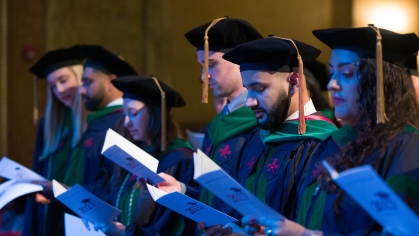 Students in graduation caps and gowns sing at convocation