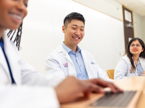 Three medical students sit at a classroom table and look at a laptop