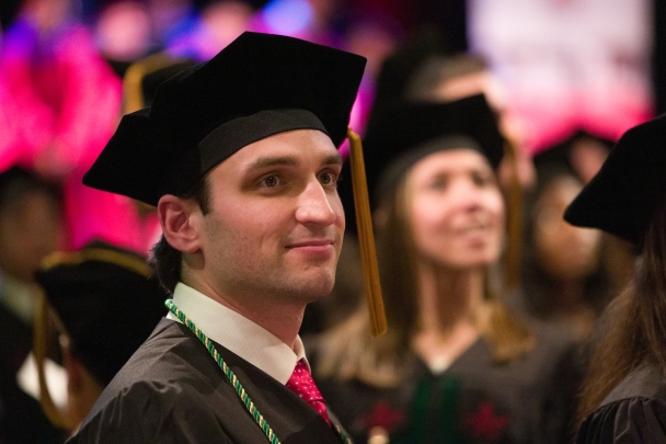 A graduate smiles at the RWJMS convocation while faculty stand on the stage in the background